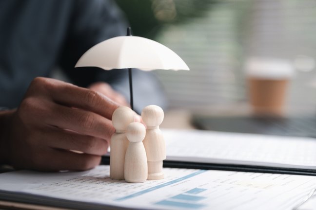 concept showing family protection with wooden figures under umbrella