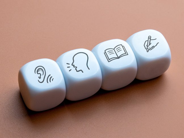 Four cubes displaying icons for listening, speaking, reading, writing skills. Language learning, education, communication