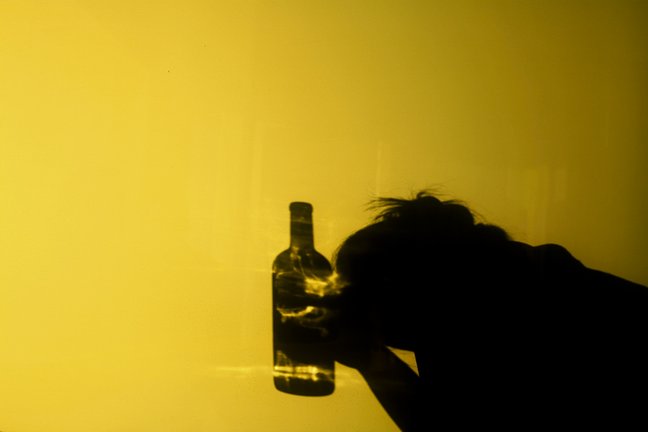 Image of an upside shadow on dim golden light, of a person holding a bottle