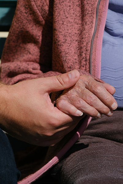 A person sitting on a bench holding their hands together, A grandson holding the hand of his grandmother with love &affection