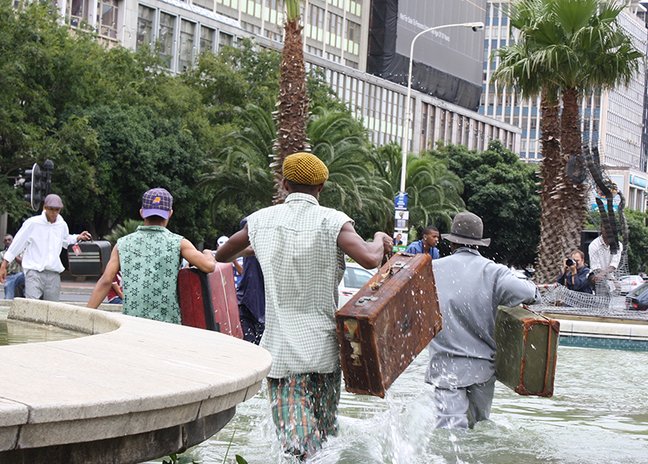 people carrying luggage running on street by water fountain